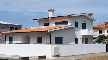 A residential building with a flat roof, multiple windows, and a visible chimney.