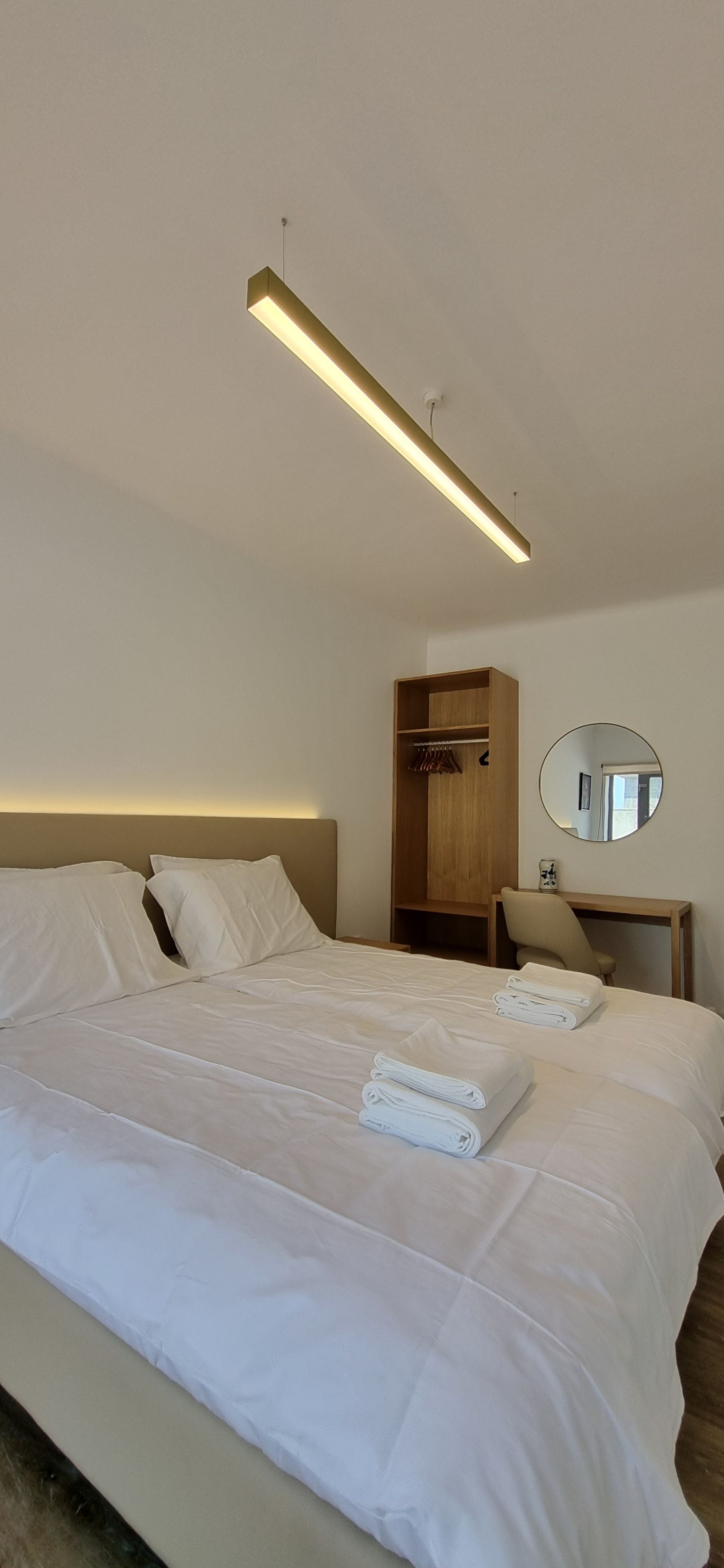 Una habitación de hotel con una cama grande, un armario de madera, un espejo redondo y una mesita de noche.