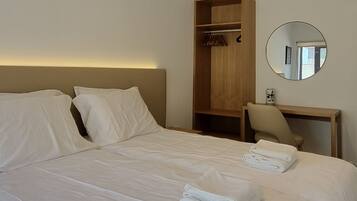 Una habitación de hotel con una cama grande, un armario de madera, un espejo redondo y una mesita de noche.