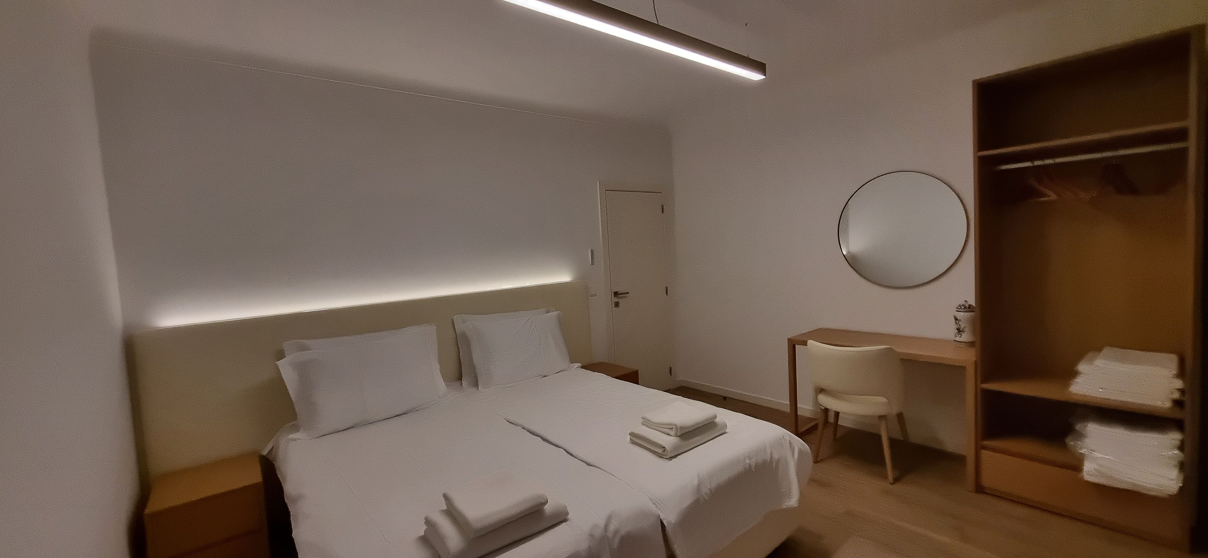 Hotellihuone, jossa on sänky, yöpöydät, työpöytä, tuoli, vaatekaappi ja peili.