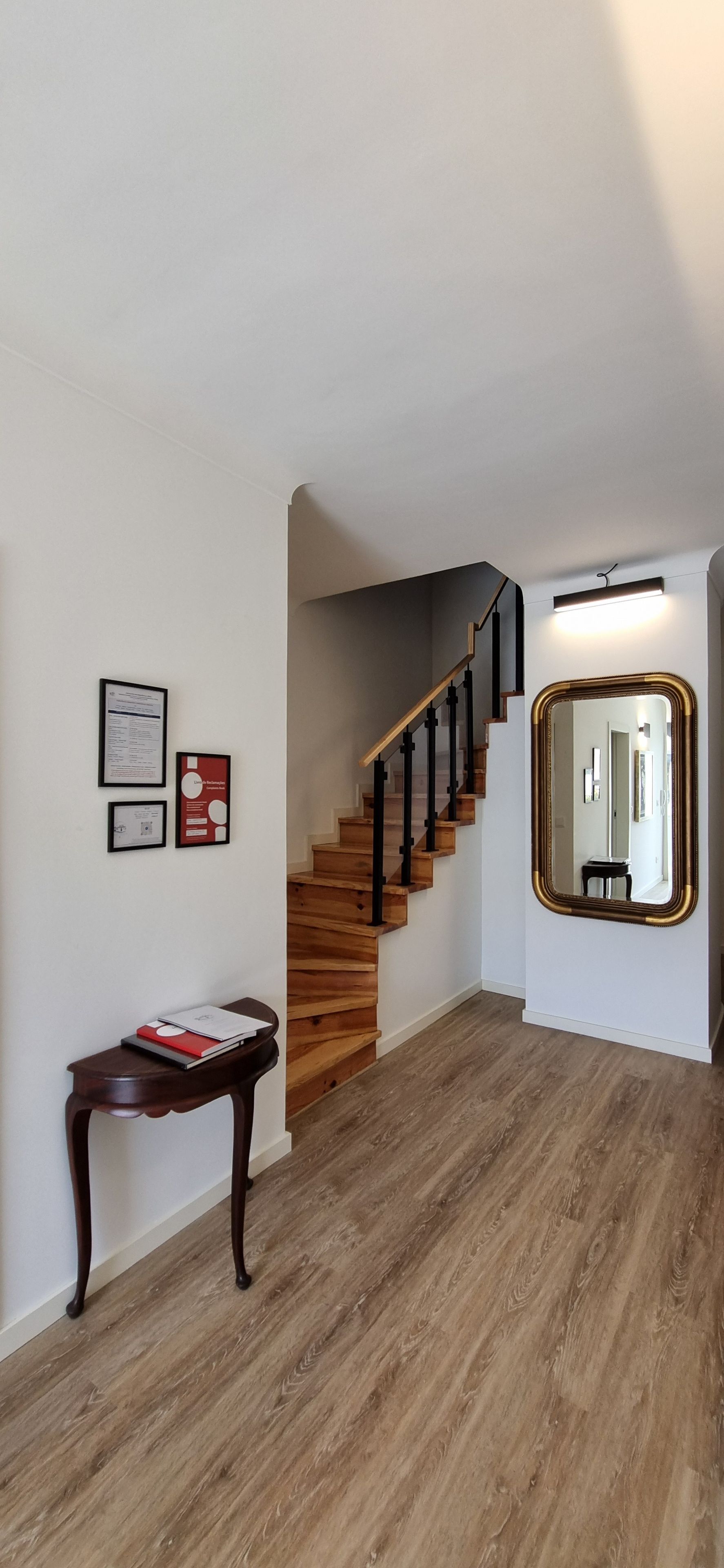 A staircase with wooden steps and black railings, a wooden console table with a red book, and a large mirror with a gold frame.