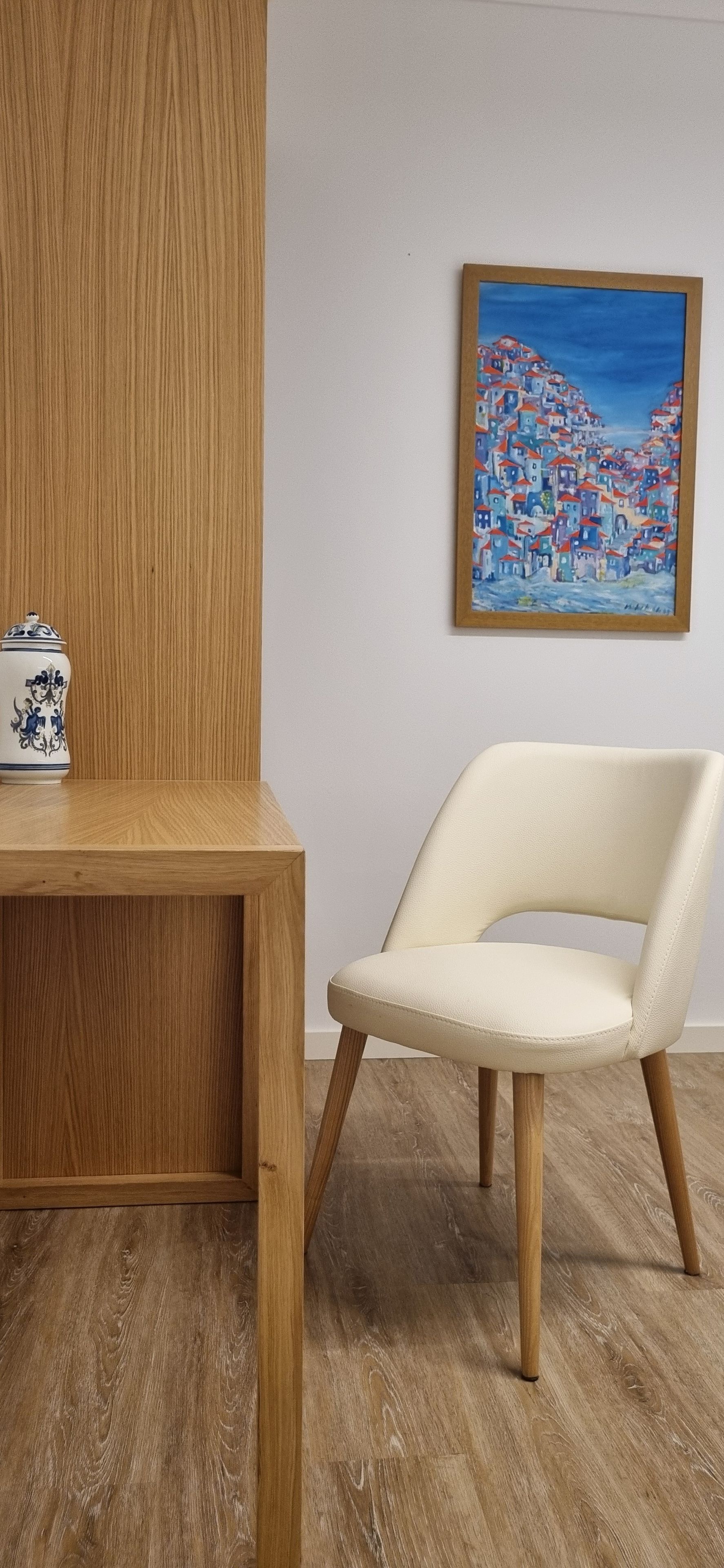 A wooden desk with a ceramic object and a white chair with wooden legs in a room with wooden flooring.