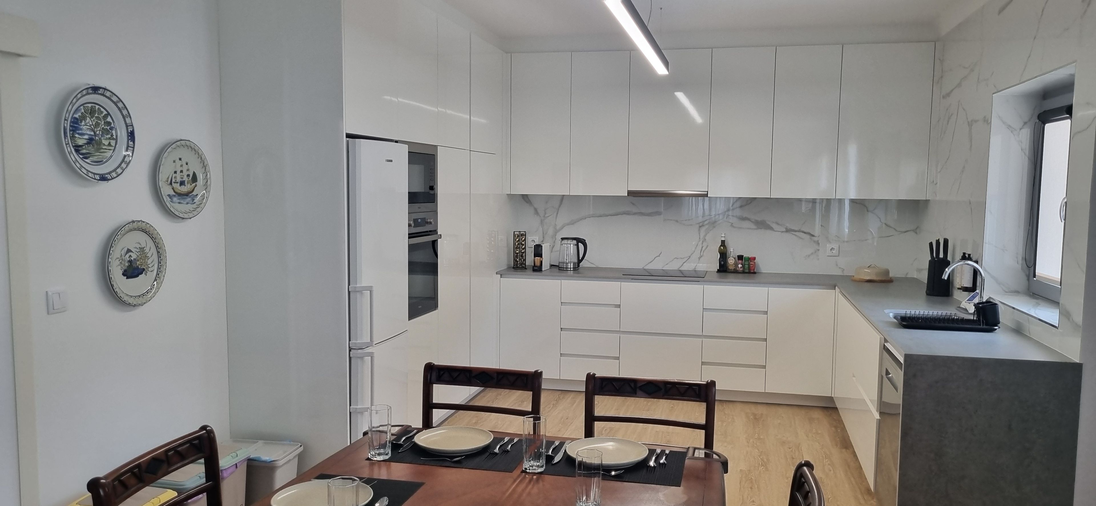 A modern kitchen with white cabinets, a marble backsplash, and a dining area with a wooden table and chairs.