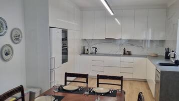 A modern kitchen with white cabinets, a marble backsplash, and a dining area with a wooden table and chairs.
