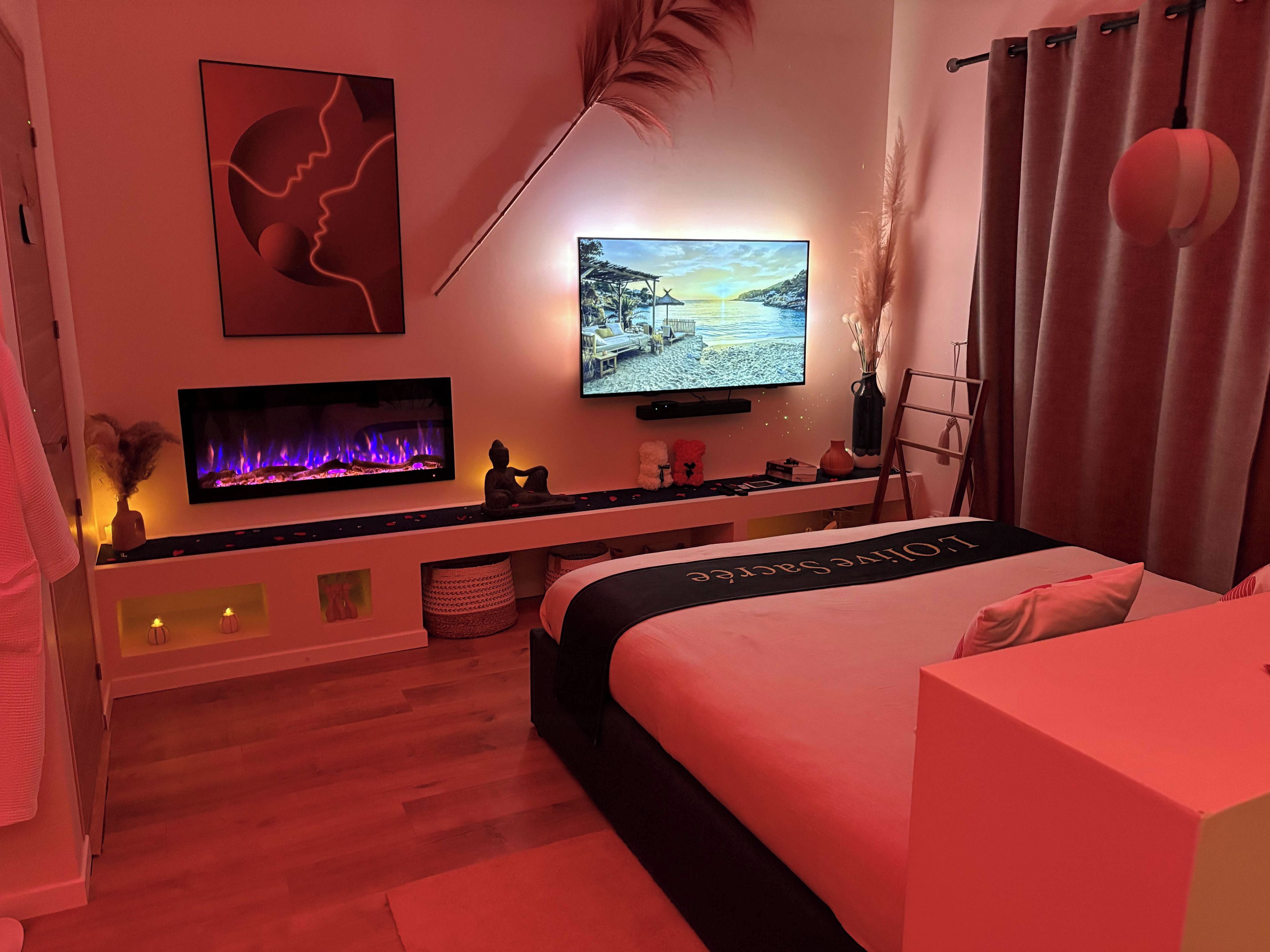 A modern bedroom with a bed, a TV, a fireplace, and a view of a sunset.