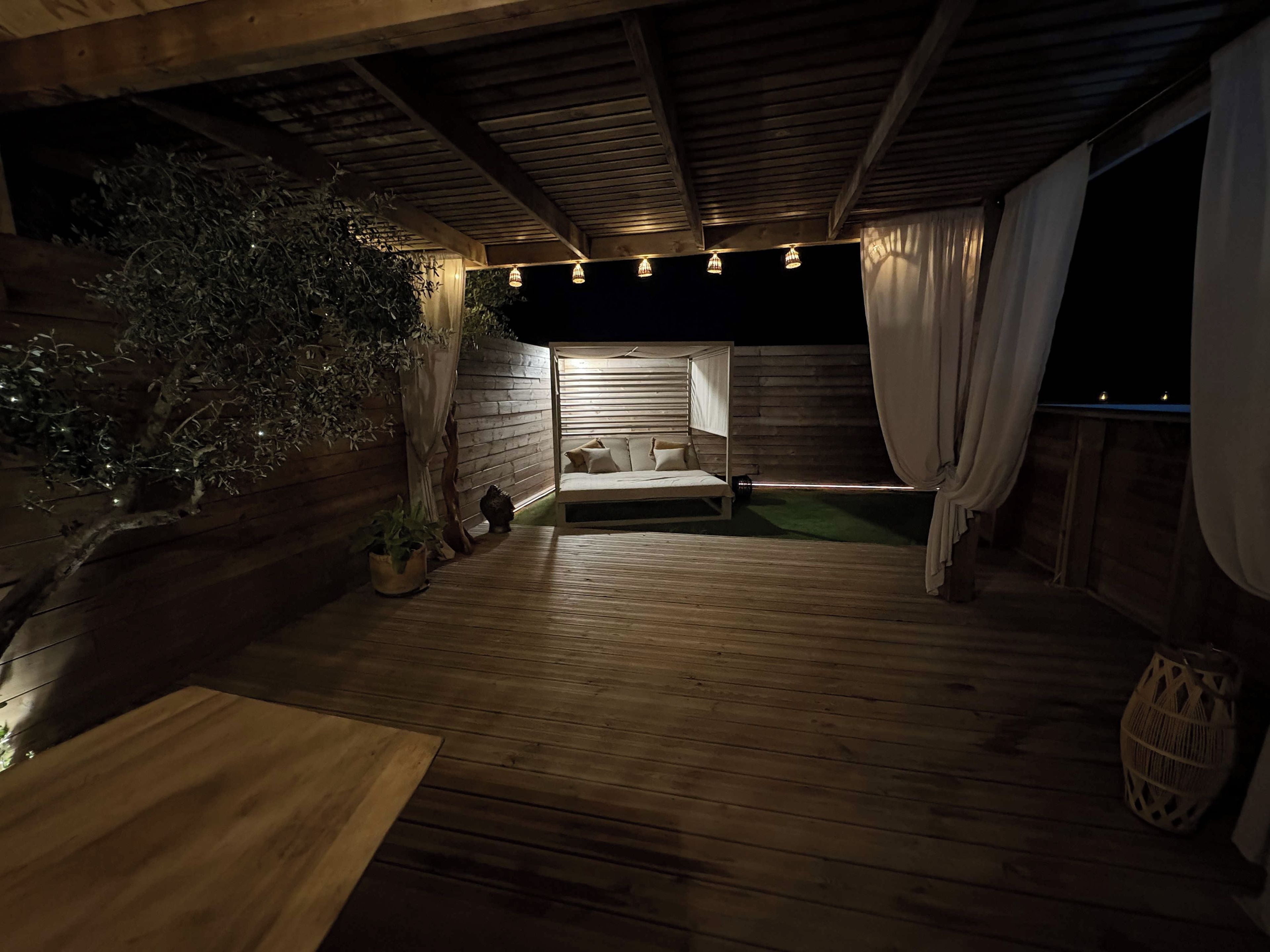 A cozy, dimly lit room with a wooden floor, a bed with white linens, and a small potted plant.