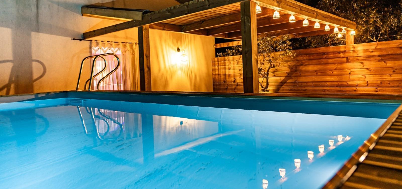 A swimming pool with a wooden deck and a covered area with lights.