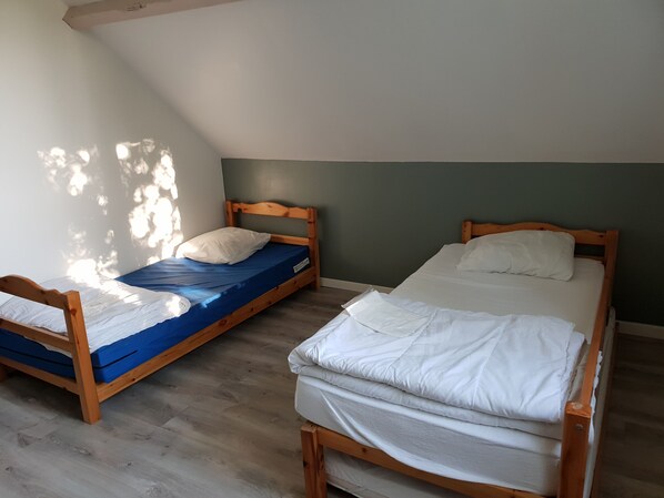 Dos camas literas de madera en una habitación con techo inclinado, suelo de madera y pared verde.