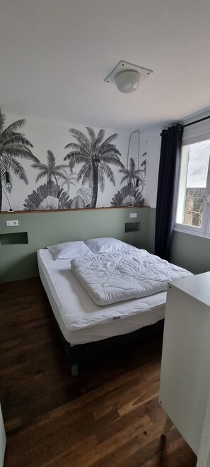 Huone, jossa on sänky, seinämaalaus, ikkuna ja kattovalaisin.