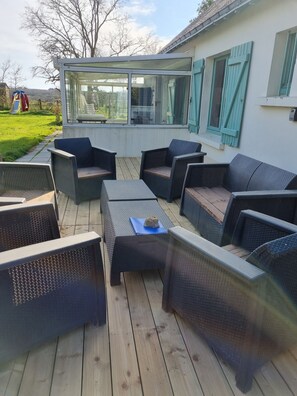 Terraza exterior con mobiliario de mimbre y cerramiento de vidrio.