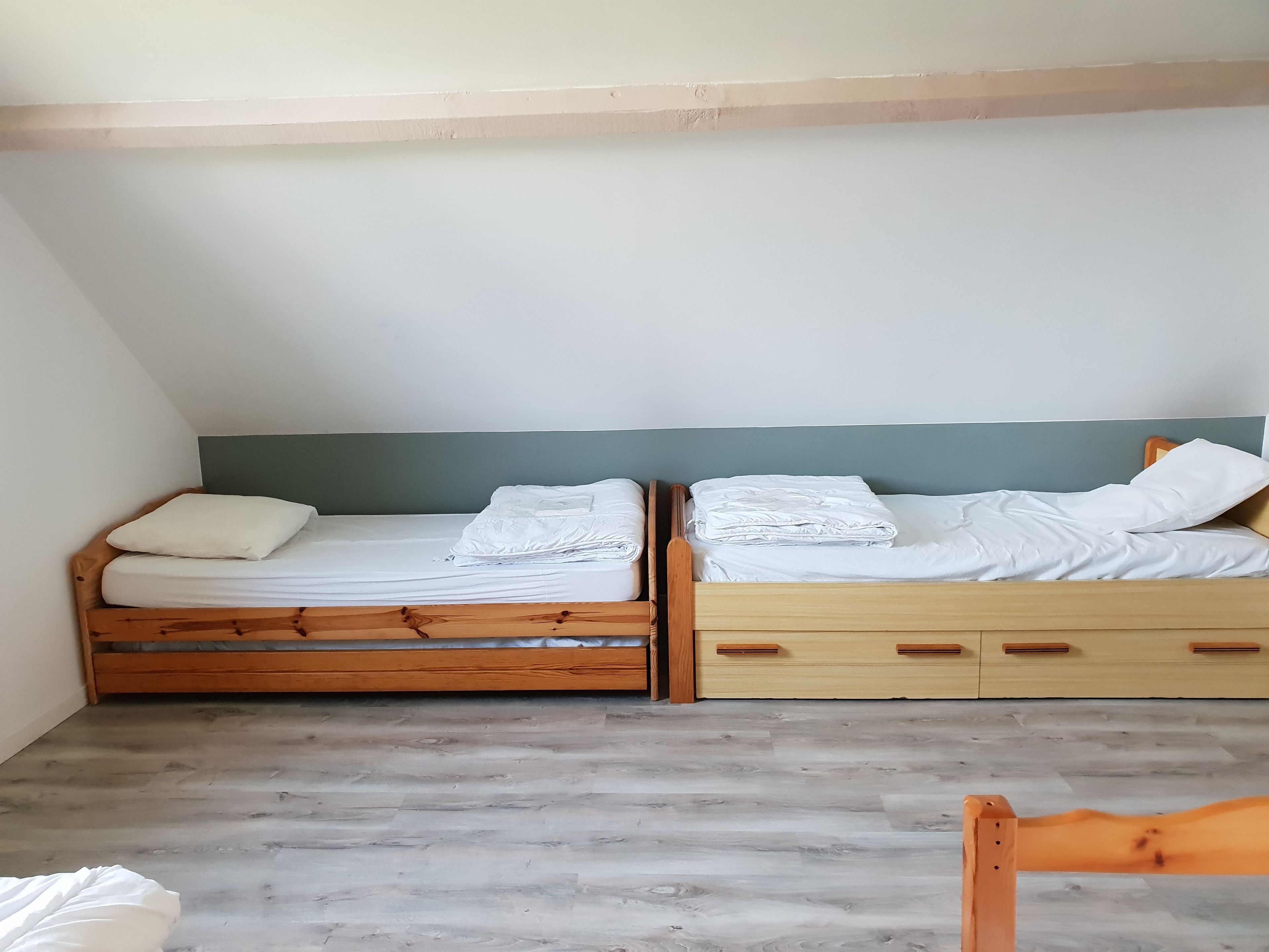 Ein Zimmer mit zwei Etagenbetten aus Holz, jeweils mit Matratze und Kissen, sowie einem Holzstuhl.