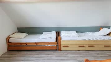 Ein Zimmer mit zwei Etagenbetten aus Holz, jeweils mit Matratze und Kissen, sowie einem Holzstuhl.