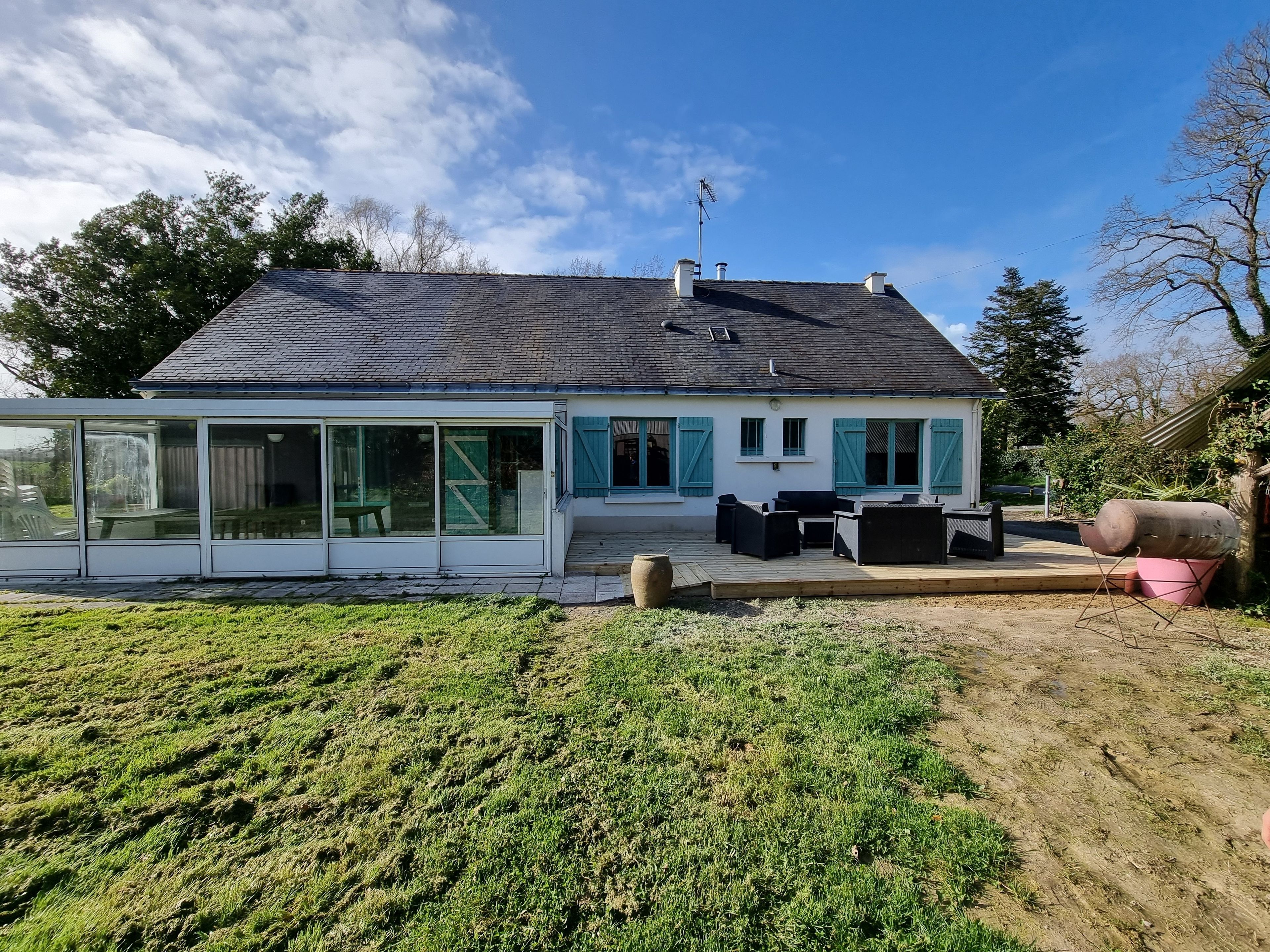 A house with a large glass extension, a deck with outdoor furniture, and a well-maintained lawn.
