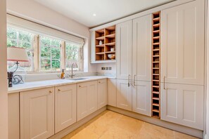 A kitchen with white cabinets, a marble countertop, a window with a view, and a built-in shelving unit. - Cotswold Cottage, Inglenook Fire & Sun-Trap Courtyard | Dog Friendly | Pub Walk (Cherington)