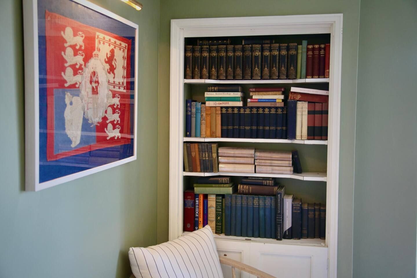 A bookshelf with various books, a framed picture on the wall, and a chair.