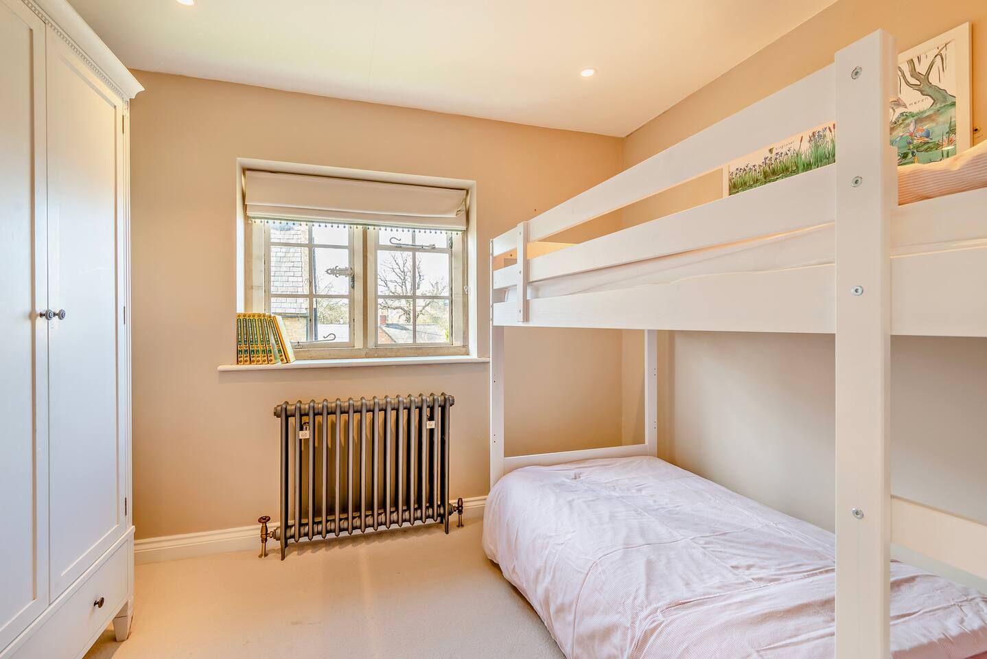 Een kinderkamer met stapelbedden, een radiator, een raam met jaloezieën en een kast.