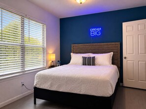 A bedroom with a bed, a nightstand, a lamp, a wall-mounted sign, and a door. - 3BR Near Morgan Wonderland With Arcade (San Antonio)