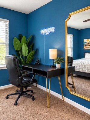 A room with a blue wall, a desk with a chair, a bed, a large mirror, and a neon sign. - 3BR Near Morgan Wonderland With Arcade (San Antonio)