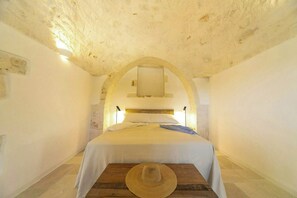 A narrow room with a bed centered under an arched ceiling, a wooden floor, and a hat on a table. - Trulli complex in the Valle d'Itria with pool (Martina Franca)