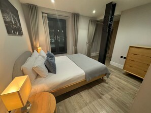 A modern bedroom with a bed, bedside table, lamp, and a wooden dresser. - City Double Viii - 2BR Home With Terrace in the City (London)