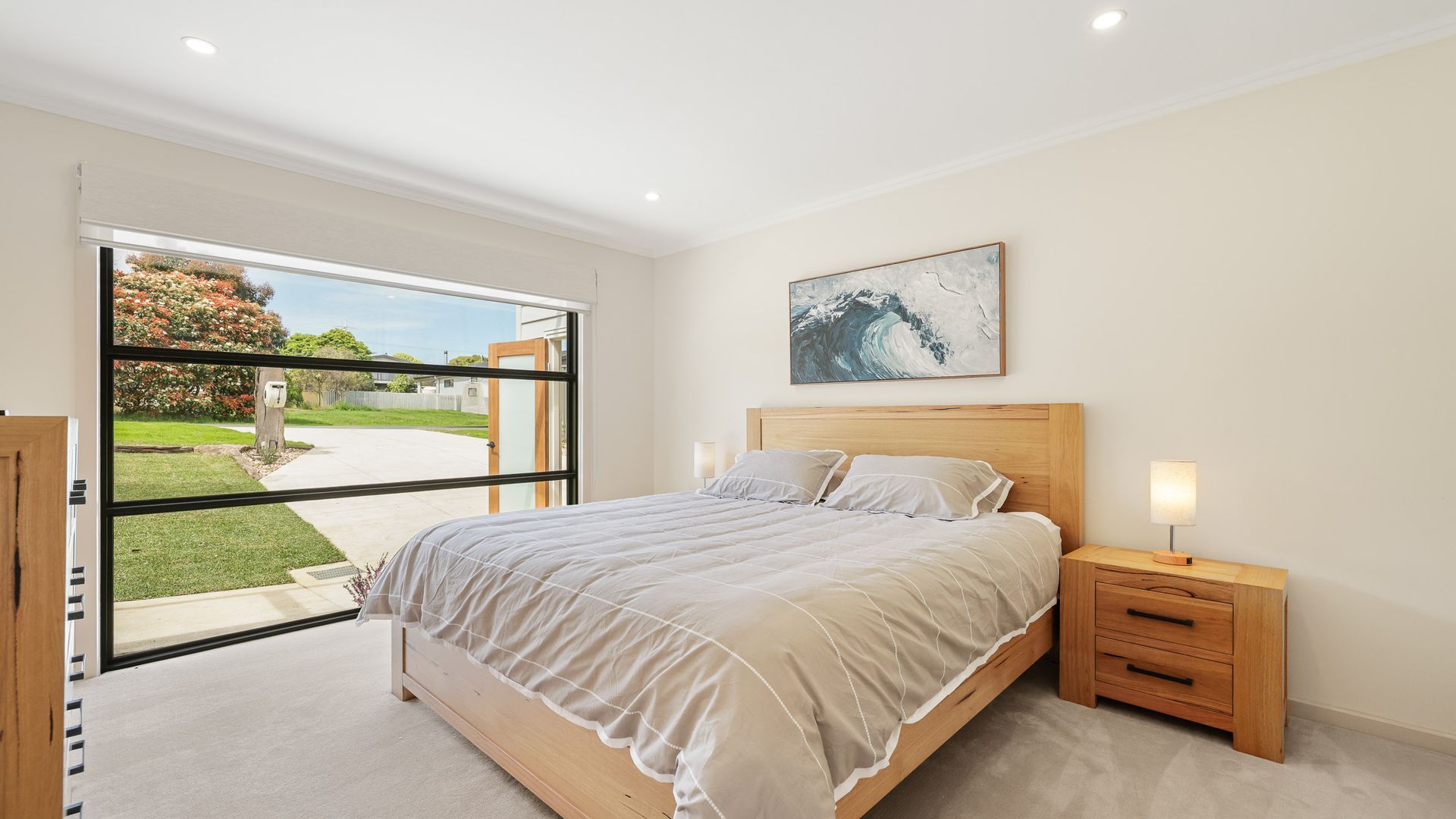 Un dormitorio con una ventana grande, una cama con cabecero de madera, mesitas de noche con lámparas y un cuadro en la pared.