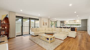 A spacious living area with a large L-shaped sofa, a wooden coffee table, and a bookshelf.