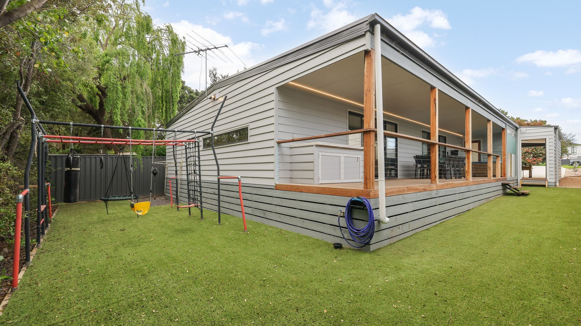 Een modern huis met een overdekte veranda, een schommel en een omheinde tuin.