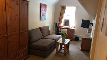 A cozy living room with a brown sofa, a small wooden table with a vase, a wooden cabinet, a television, and a window with curtains.