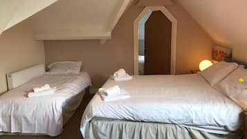 A room with two beds, each with a pillow and a rolled towel. There is a radiator under one bed and a lamp on the nightstand.