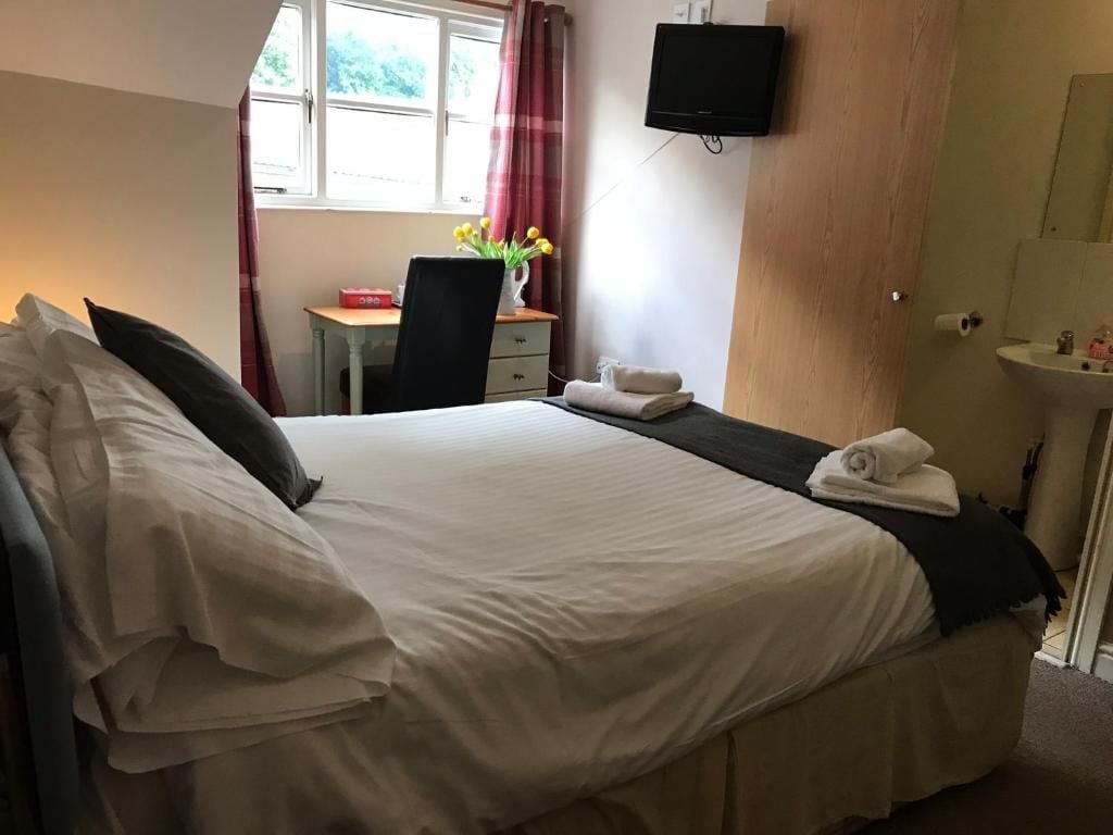 A hotel room with a bed, a desk with a chair, a TV mounted on the wall, and a window with curtains.