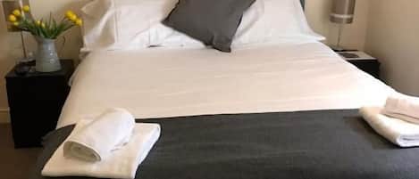 A neatly made bed with white and black bedding, a vase with flowers, and a wall art piece.
