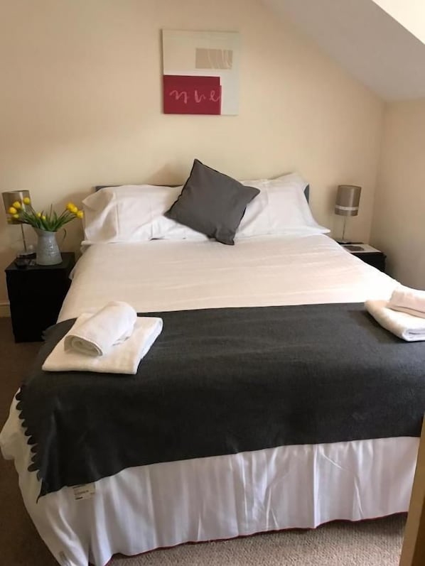 A neatly made bed with white and black bedding, a vase with flowers, and a wall art piece.