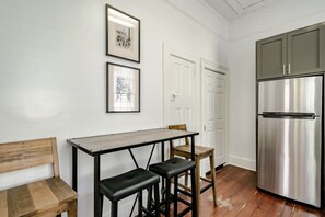 A kitchen with a stainless steel refrigerator, a wooden bench, two stools, and framed pictures on the wall. - Betty (Mobile)