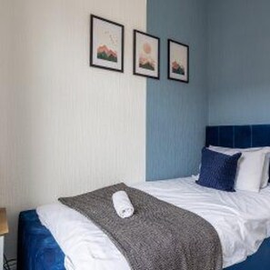 A hotel room with a bed, a blue headboard, and three framed pictures on the wall. - Central Blyth - House - Sleeps 5 - Seaside (Blyth)