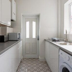 A compact kitchen with white cabinets, a microwave, and a washing machine. - Central Blyth - House - Sleeps 5 - Seaside (Blyth)