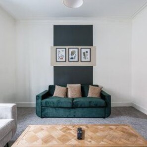 A room with a dark green sofa, a wooden coffee table, and three framed artworks on the wall. - Central Blyth - House - Sleeps 5 - Seaside (Blyth)