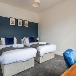 A hotel room with two beds, a blue accent wall, and a grey carpet. - Central Blyth - House - Sleeps 5 - Seaside (Blyth)