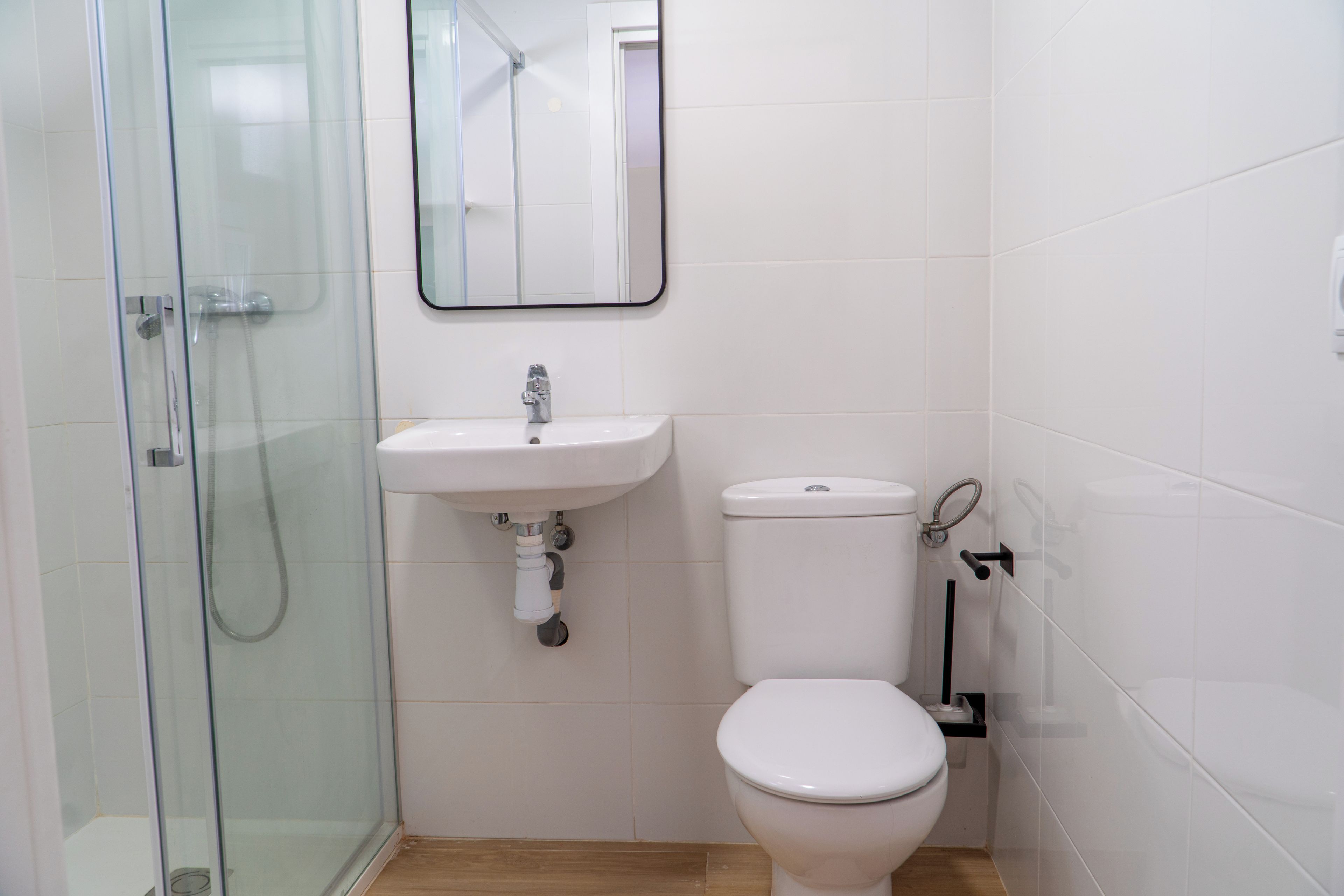 Een badkamer met een douchecabine van glas, een witte wastafel en een toilet.
