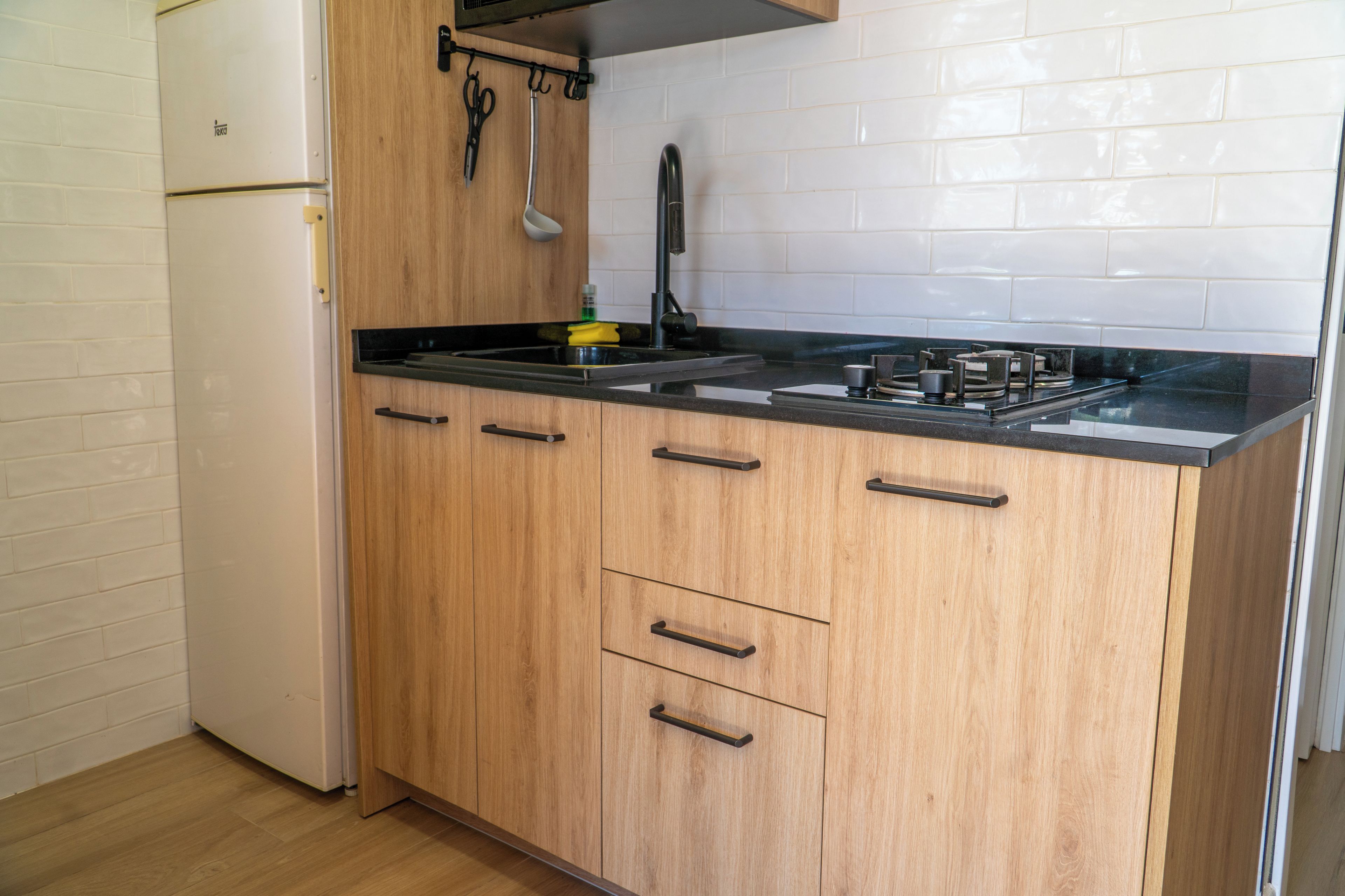 Een keuken met houten kastjes, een zwart aanrecht en een witte koelkast.