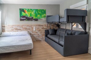 A compact room with a bunk bed, a single bed, and a stone-patterned wall.