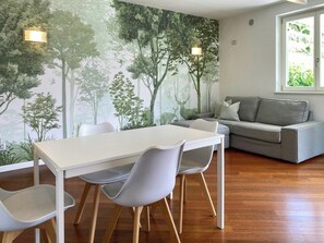 A modern living room with a dining area, a grey sofa, and a mural of a forest. - View over Lake Caldonazzo with large terrace (pergine valsugana)