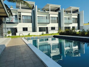 A modern residential building with a swimming pool, balconies, and a gated entrance.
