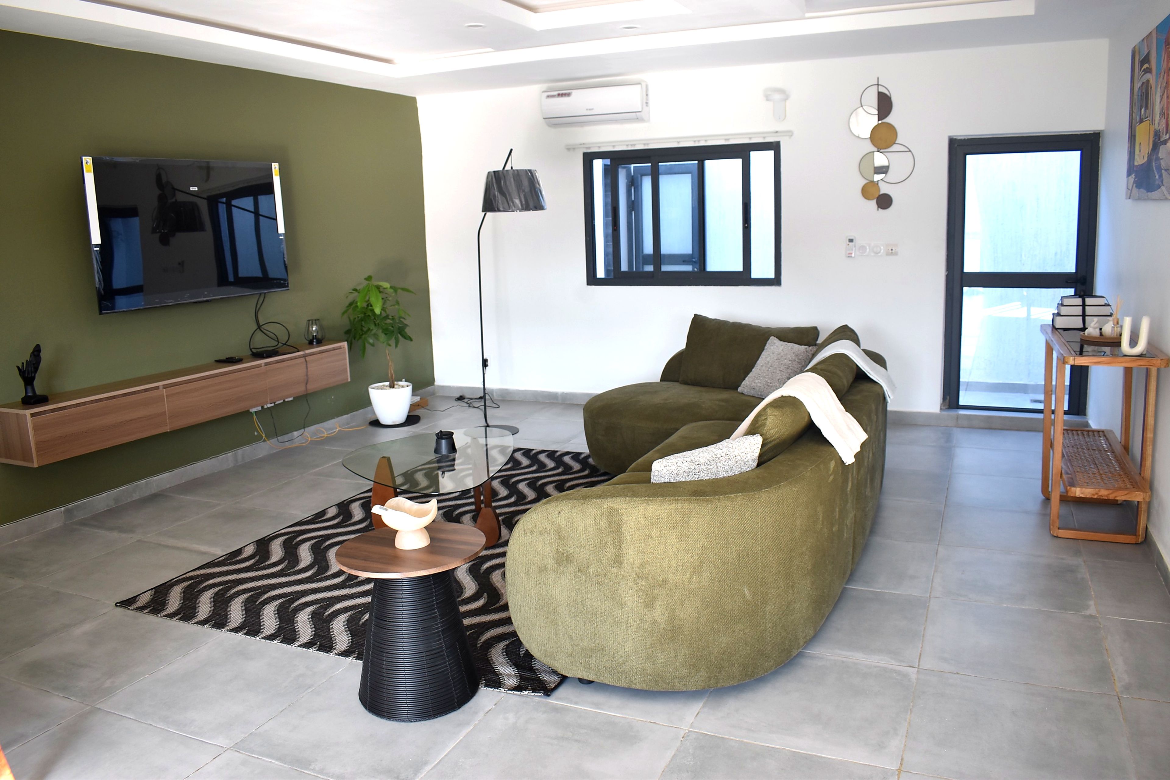 A modern living room with a curved sofa, a glass coffee table, and a television mounted on the wall.