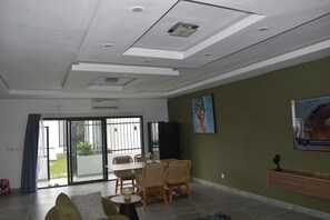A modern living room with a sofa, a dining table with chairs, a TV, and a painting on the wall.