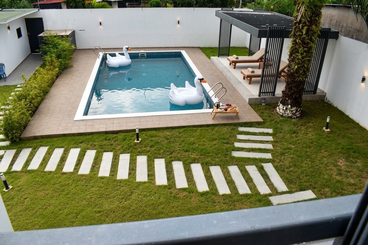 Une piscine avec des bouées en forme de cygne, un espace détente avec des fauteuils et un palmier.