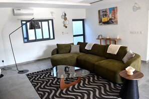 A living room with a sofa, a glass coffee table, a patterned rug, a painting, and a small table with a decorative item.