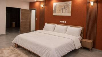 A modern bedroom with a large bed, a wooden headboard, a nightstand, and a wall-mounted light fixture.