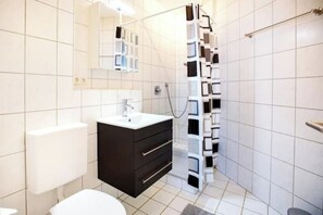 A modern bathroom with a white toilet, a black vanity with a mirror, and a shower with a white and black tiled design. - Schöne, moderne Wohnung in Stadtnähe (Würzburg)