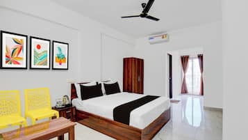 A hotel room with a bed, a desk, chairs, artwork on the wall, and a ceiling fan.