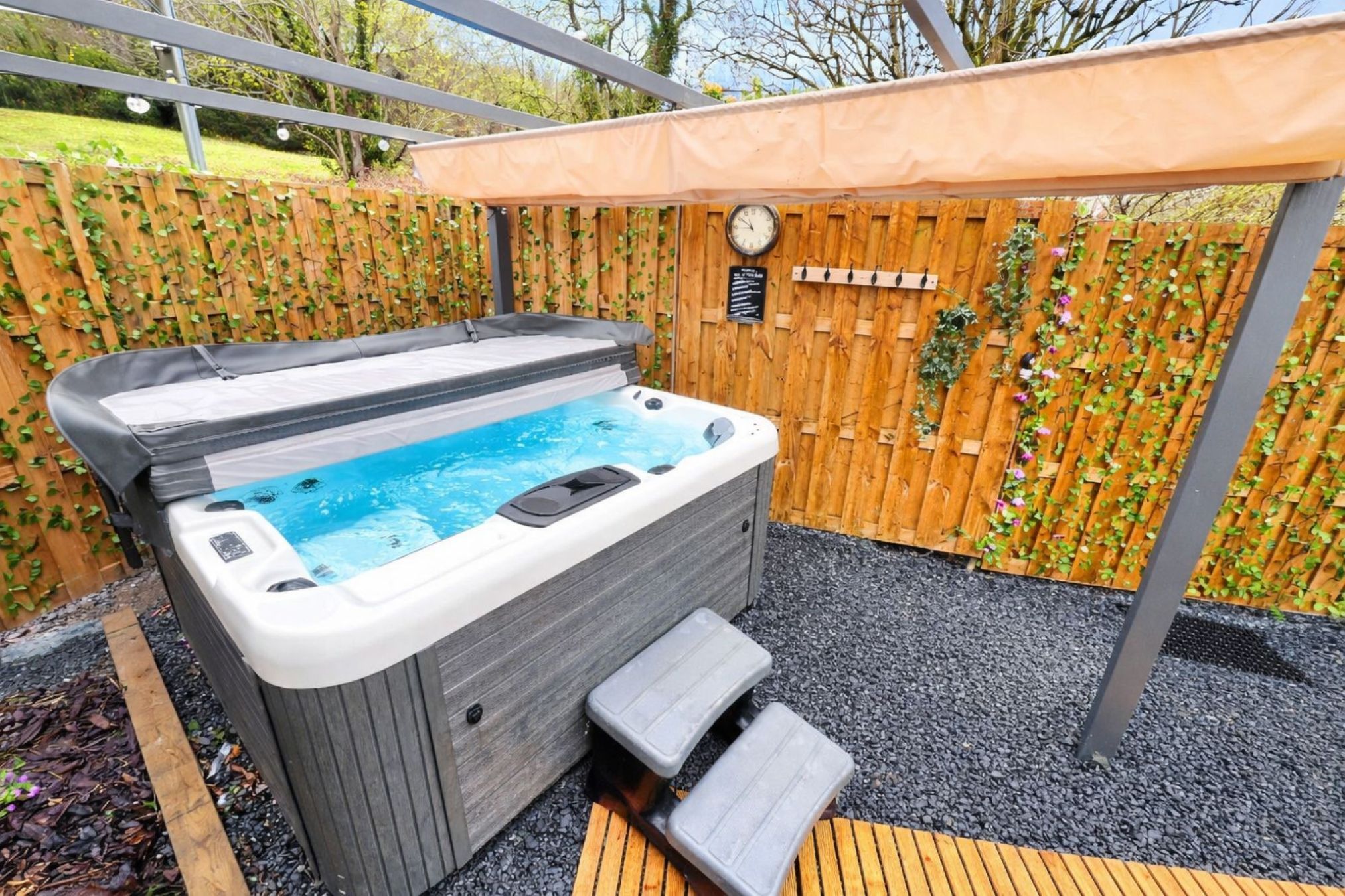 A hot tub with a wooden deck and a wooden fence with climbing plants.